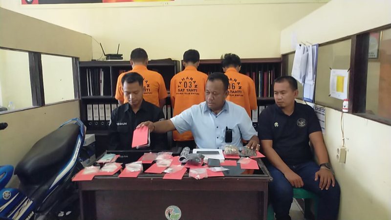 KBO Sat Narkoba Ipda Hery didampingi Kasi Humas Ipda Teguh dan Penyidik Pembantu Bripka Kasmin Musa tampak depan bersama barang bukti , dan tampak dibelakang tiga tersangka mengenakan baju berwarna kuning.