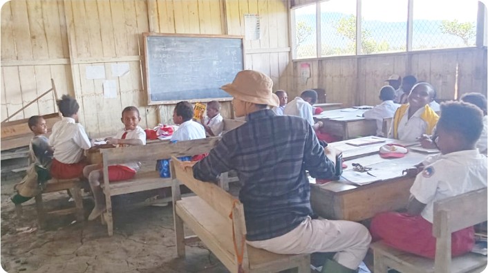 Tampak seorang guru SD Negeri Wowarek, Desa Eragama, Distrik Kurulu, Kabupaten Jayawijaya, Provinsi Papua Pegunungan, sedang menjalankan tugasnya. Terlihat pula suasana para guru yang mengajar di ruang kelas serta kondisi bangunan sekolah SD Negeri Wowarek.