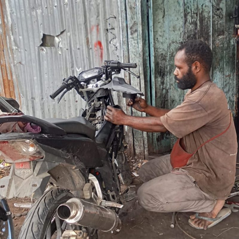 Pengusaha otomotif di Wamena, Semi Pabika, tampak sedang memperbaiki motor.
(Foto: Julianus Surabut/MPR)  
